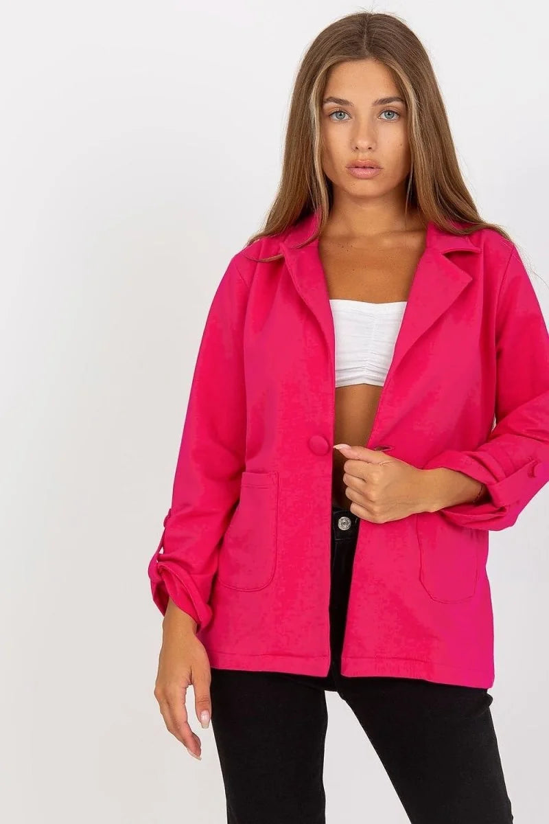 A woman wears a fuchsia blazer with rolled sleeves and front pockets over a white crop top.