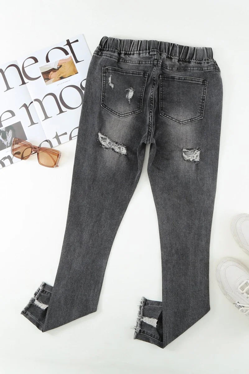 Distressed charcoal grey denim jeans with a frayed hem and elastic waistband, shown flat lay.