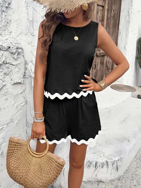Black sleeveless top with scalloped white trim and matching shorts, worn by a model holding a straw bag.
