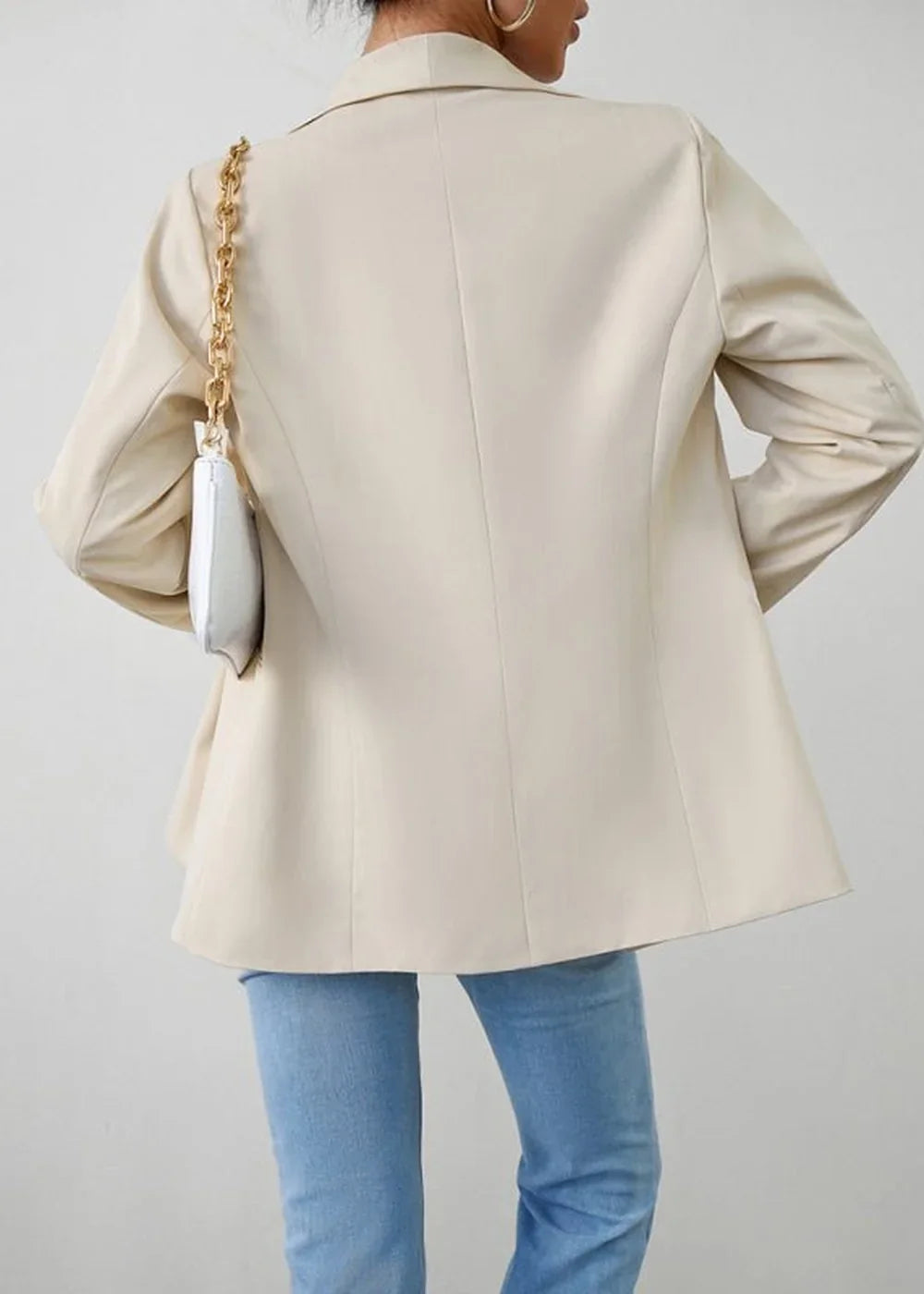 Back view of a cream blazer on a model, paired with light wash jeans and a white clutch with a gold chain strap.