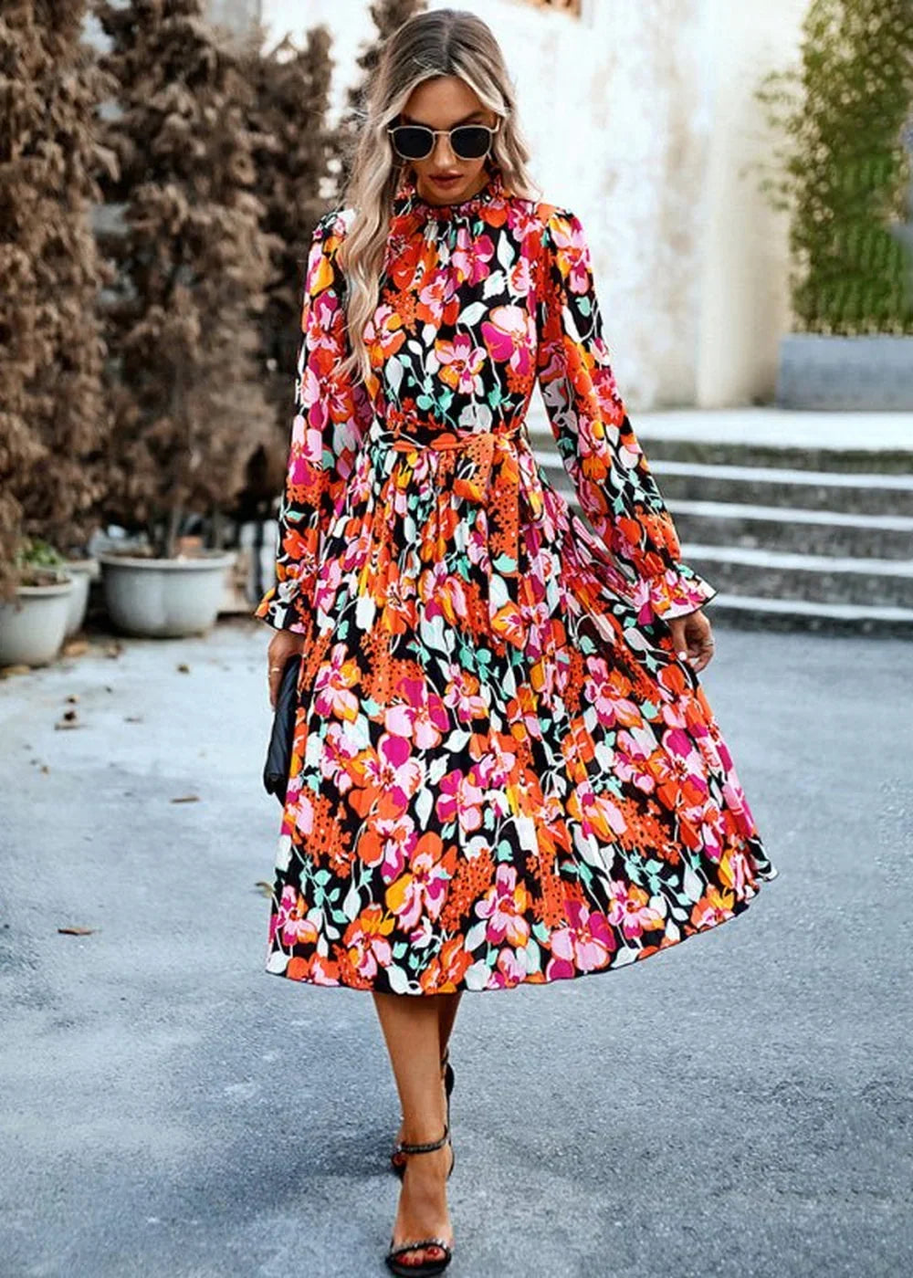 A woman walks forward in a vibrant floral print midi dress with a ruffled neckline and long sleeves.