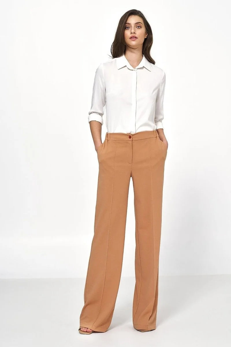 Full-length shot of a woman wearing relaxed-fit, camel-colored wide-leg trousers with a white collared shirt.