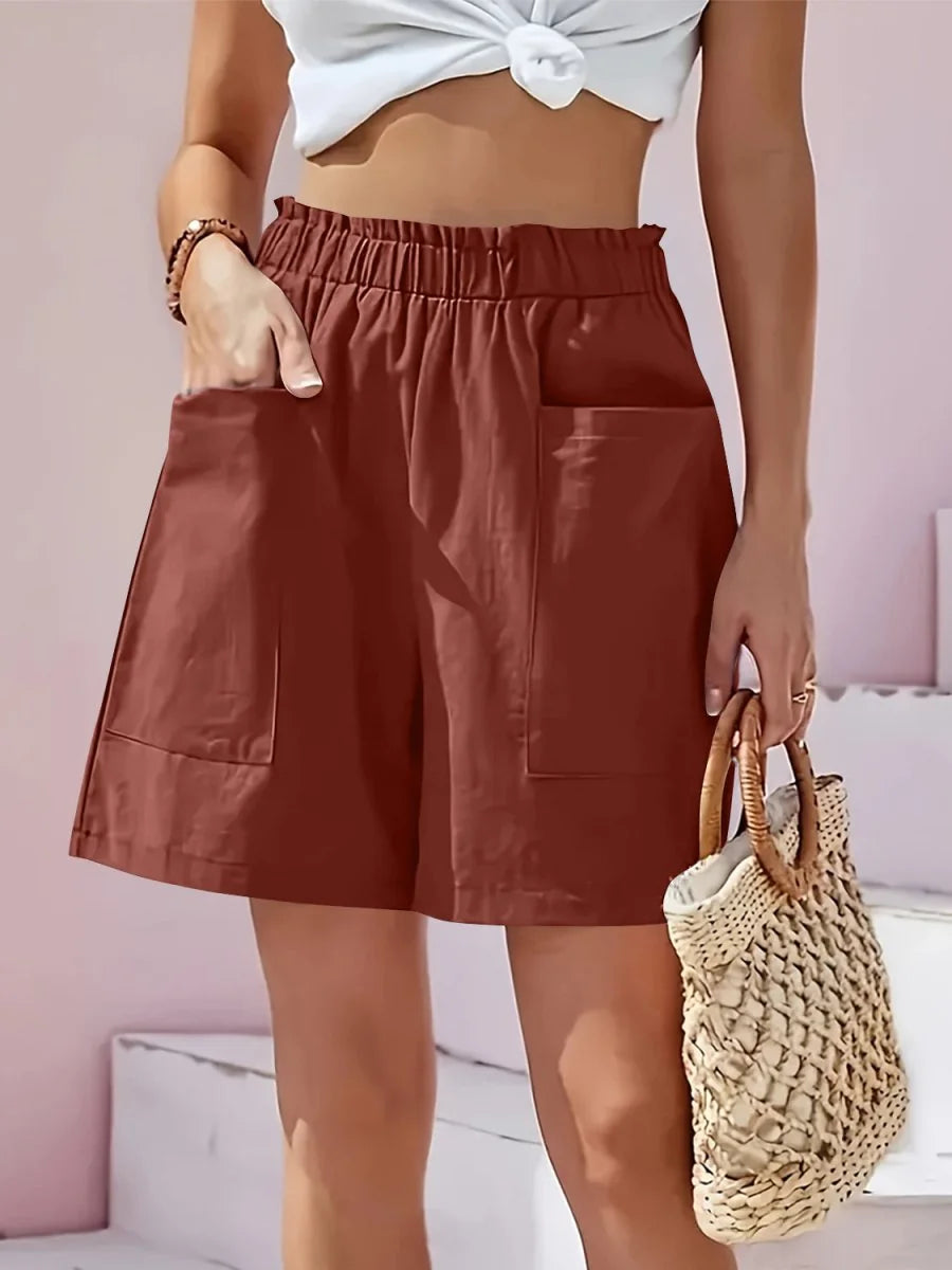 Rust-colored shorts with elastic waistband, pockets, and a straw bag.
