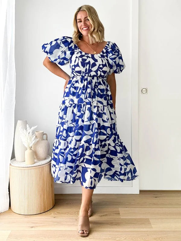Woman in a blue and white abstract print midi dress with puff sleeves and tiered skirt.