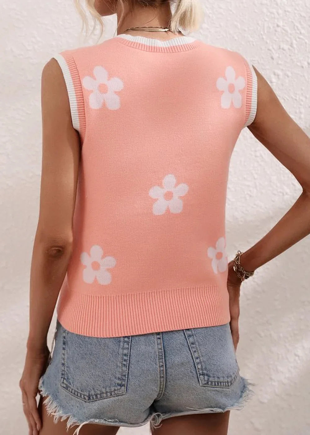 Back view of a peach knit vest with a white floral pattern and white trim at the neck and armholes.
