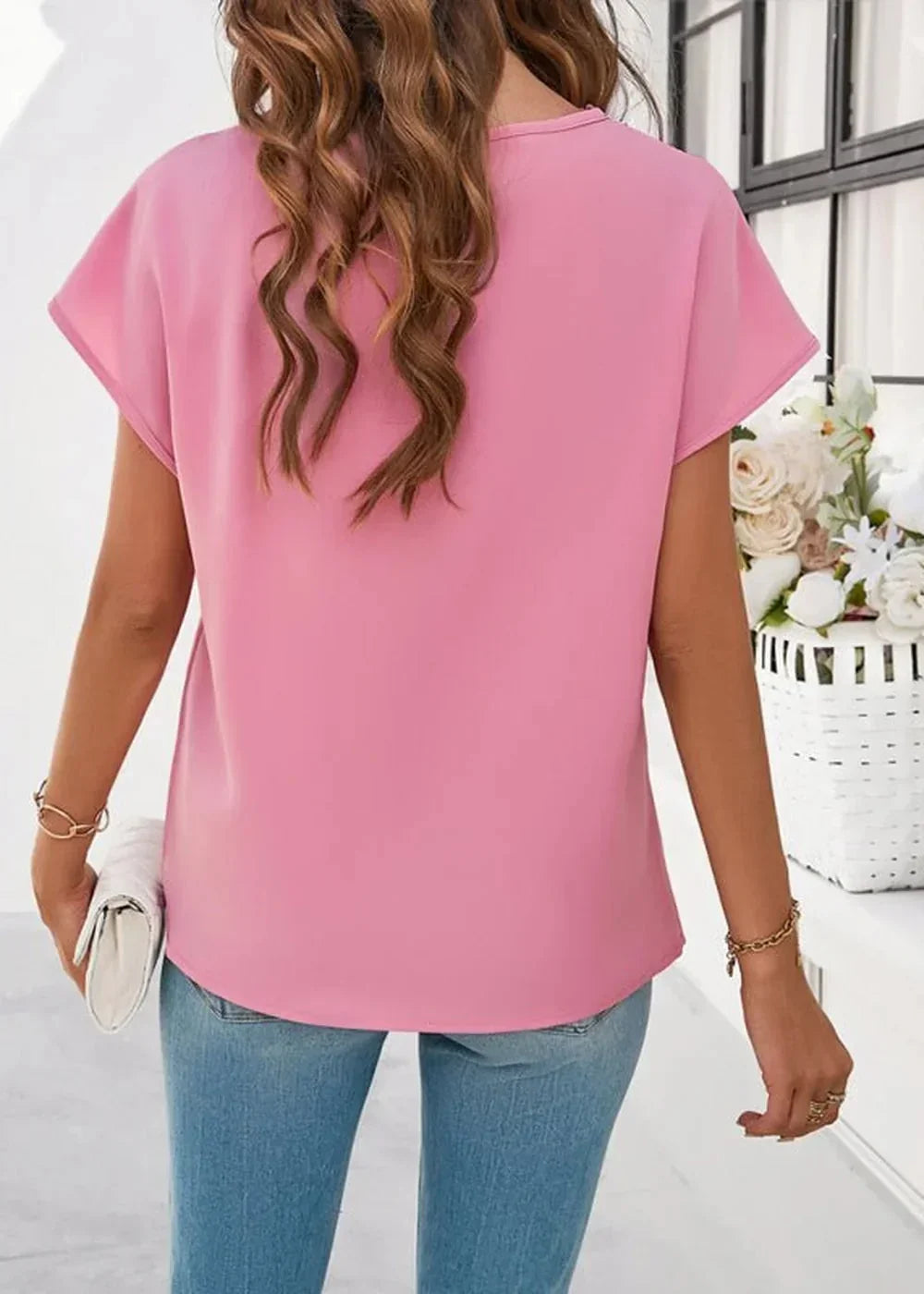Back view of a pink short-sleeve top worn by a model with blue jeans.