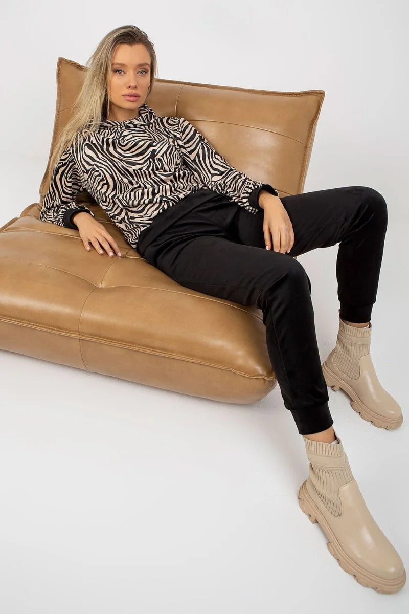 Woman wearing black joggers with a zebra print hoodie, seated on a tan leather chair.