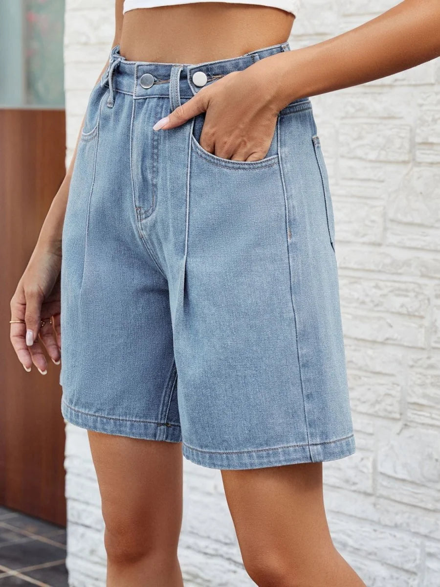 Light wash denim shorts with a relaxed fit and pleats at the waist, showing a hand in the pocket.