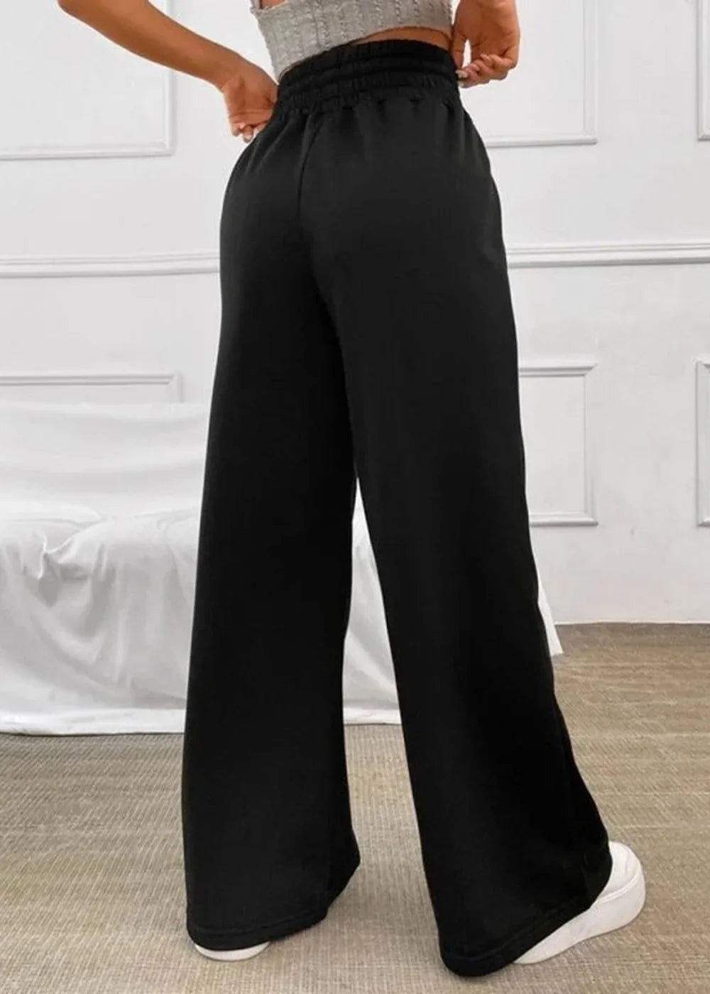 Black wide-leg pants with a cinched waist, shown from the back on a model wearing white sneakers.