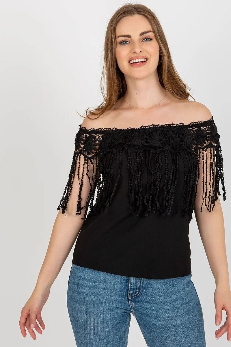 Black off-the-shoulder top with crochet trim and fringe detail, paired with blue jeans.
