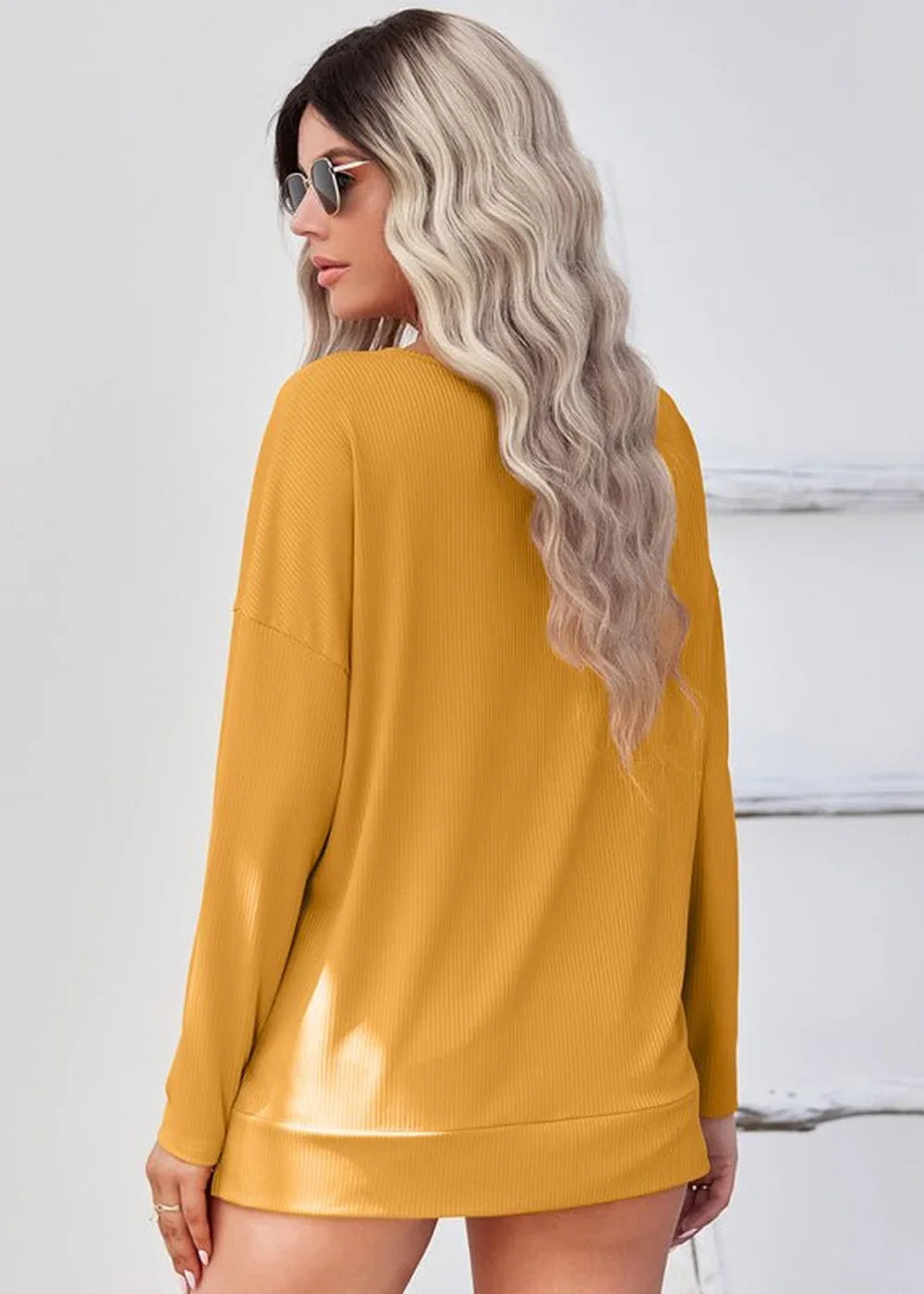 Back view of a woman wearing a mustard yellow ribbed long-sleeve top with sunglasses