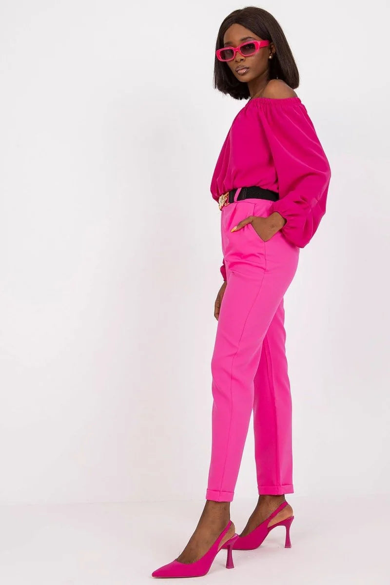 Woman in a bright pink off-the-shoulder top and matching pink pants with a black belt, wearing pink slingback heels.