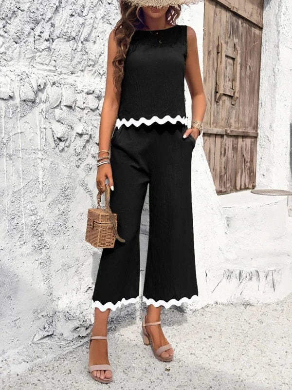 Black sleeveless top and wide-leg pants with scalloped white trim, on a model.
