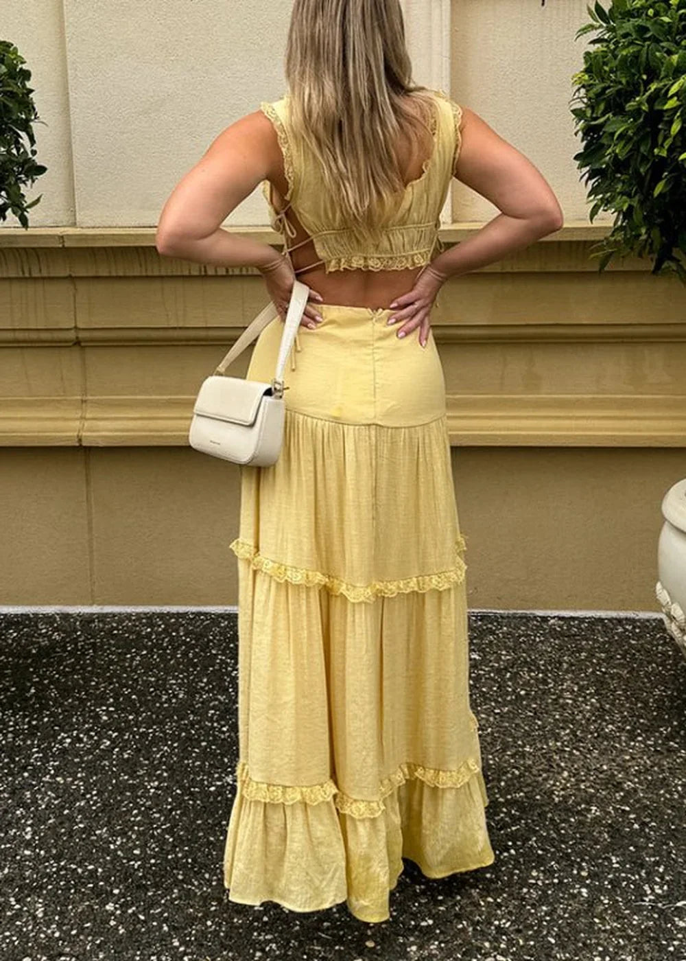 Back view of a pale yellow tiered maxi skirt with lace trim and a white crossbody bag.