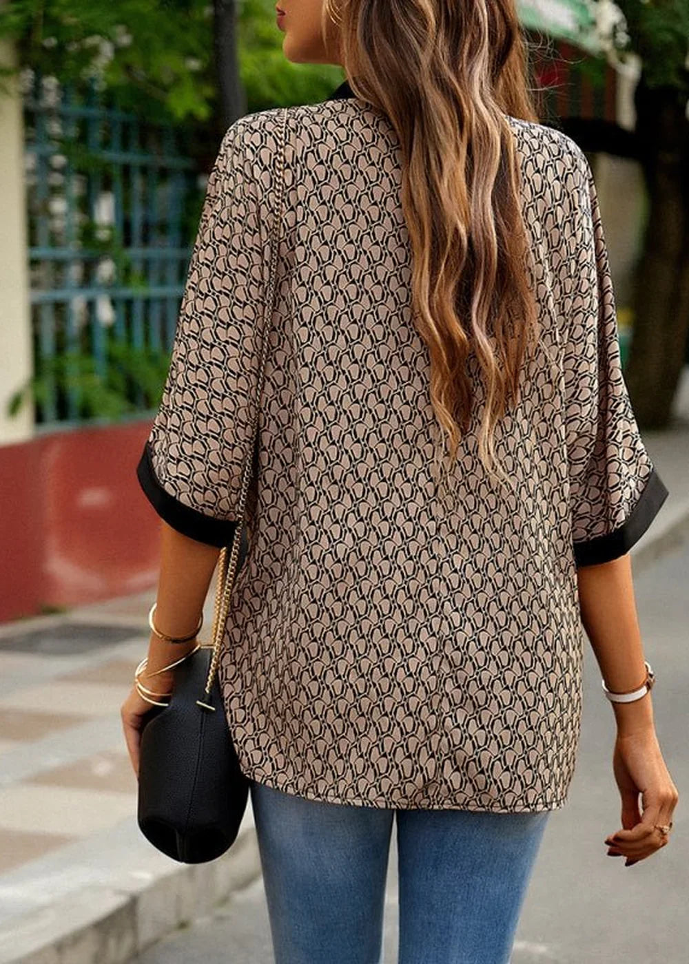 Woman from back wearing a tan and black patterned polyester top and blue jeans.