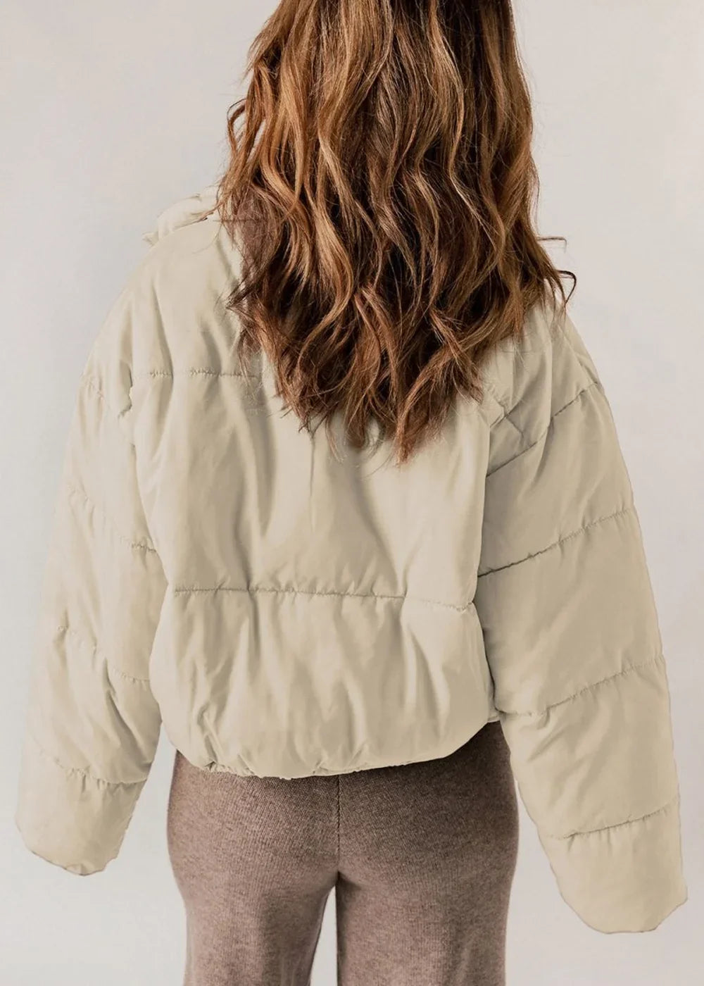 Back view of a cream puffer jacket with textured fabric and brown ribbed pants on a model.