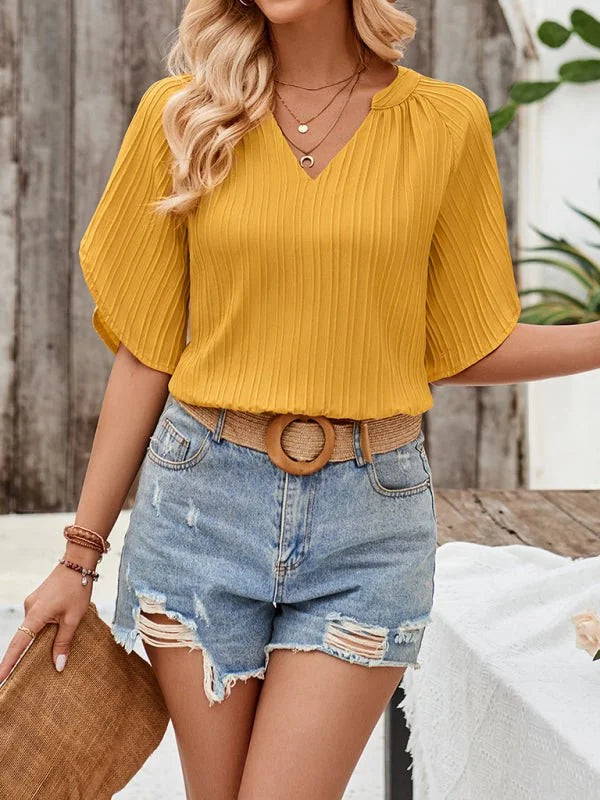 Yellow pleated blouse with V-neck and short sleeves, paired with distressed denim shorts and a woven belt.