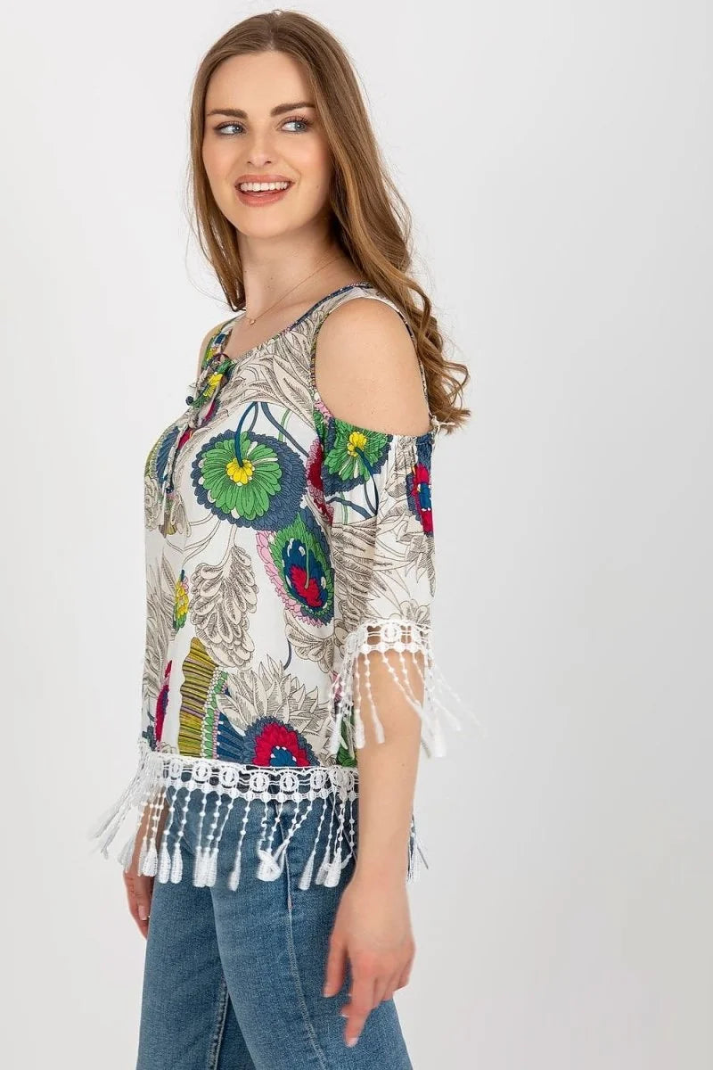 White cold-shoulder top with colorful floral print and white fringe trim on sleeves and hem.