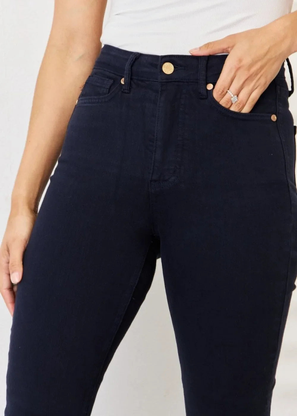 Close-up of navy blue cotton blend jeans showing gold button details and a woman's hand with a ring in the pocket.