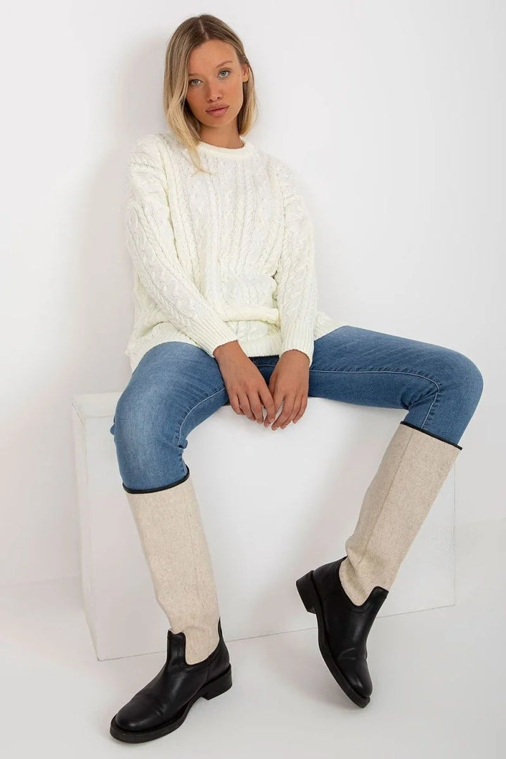 Cream cable knit sweater over blue jeans with black and cream boots.
