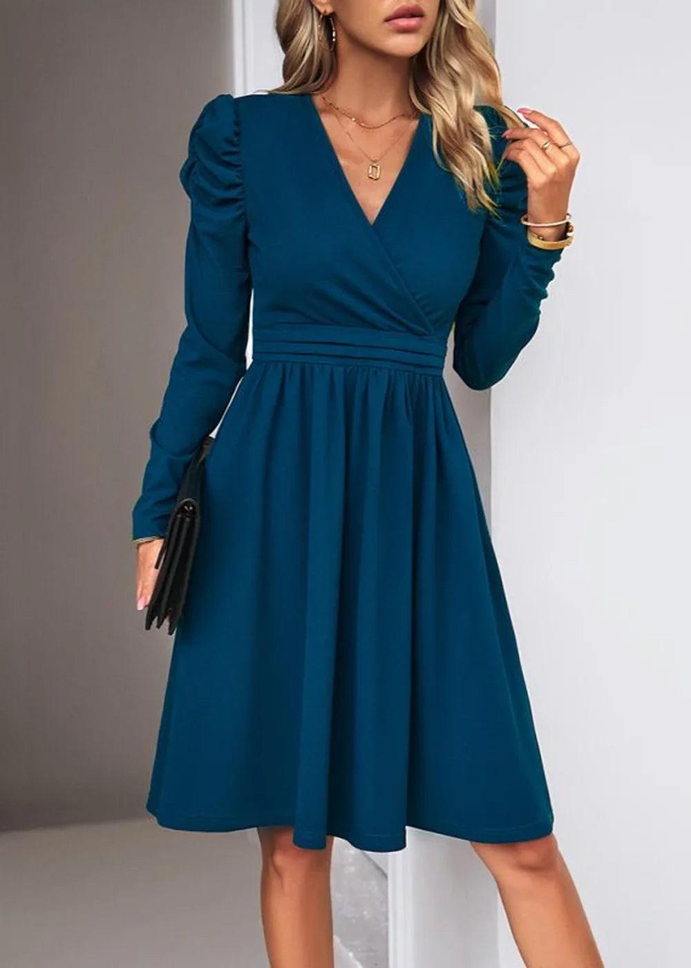 Teal V-neck dress with ruched sleeves, cinched waist, and flowing skirt, held by a woman with a clutch.