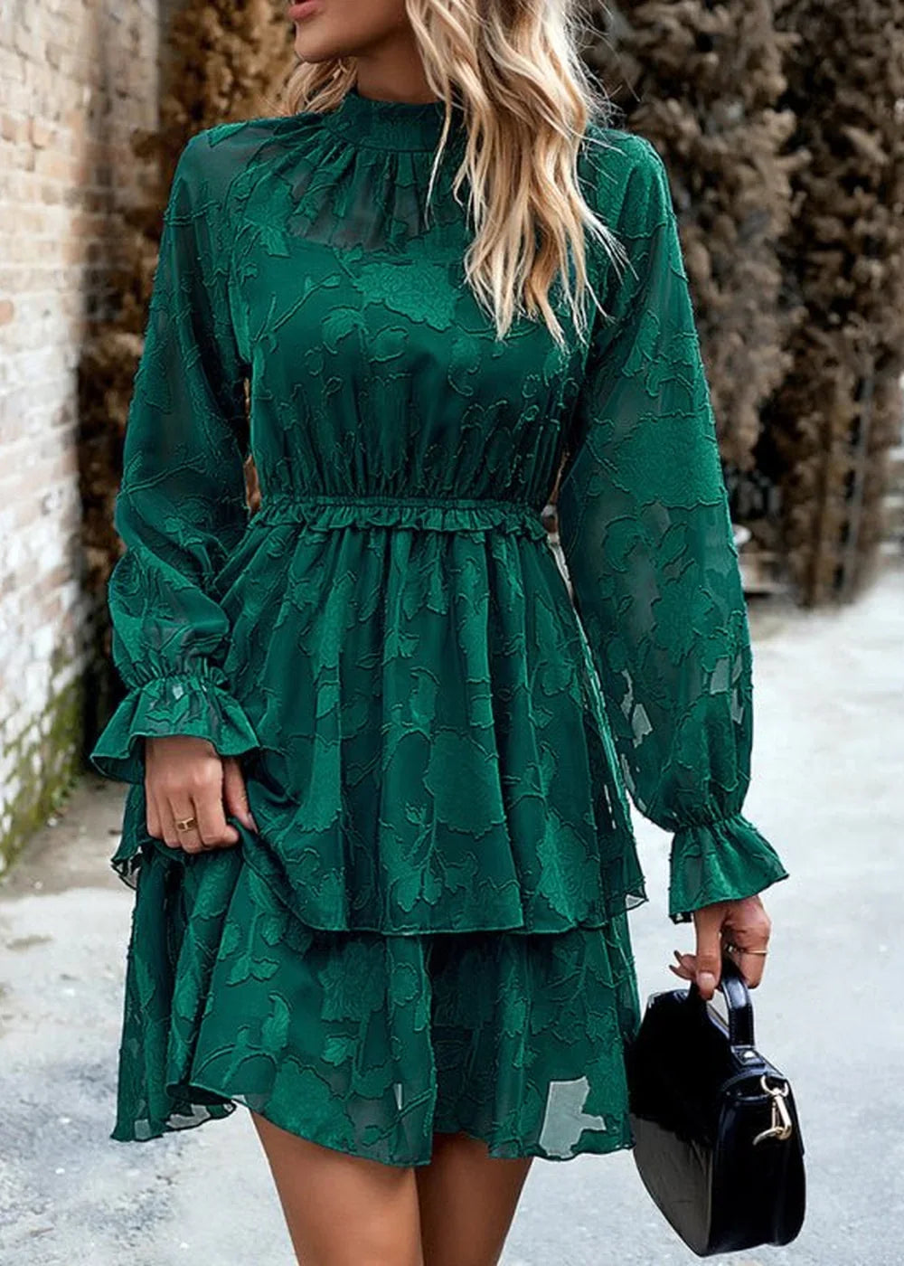 Emerald green lace tiered mini dress with ruffled cuffs and high neckline on model holding black handbag.