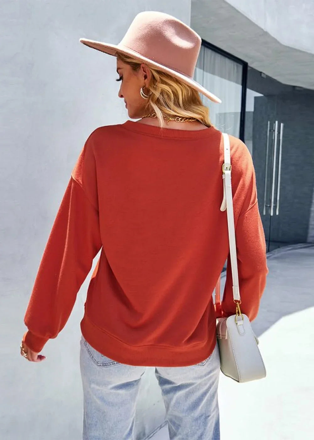 Back view of a woman wearing a rust-colored, loose-fit long-sleeve sweatshirt and light wash jeans.