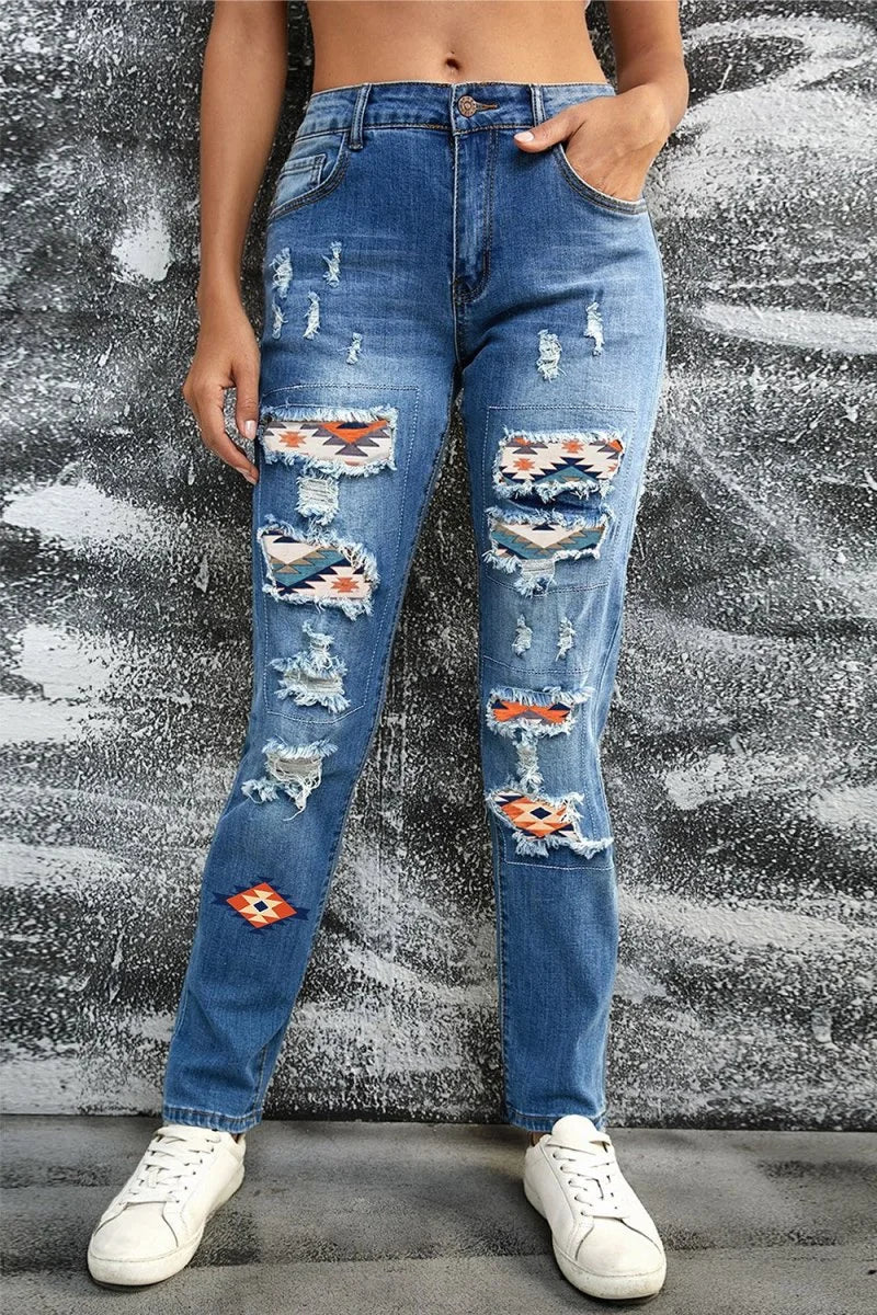 Distressed blue denim jeans with colorful geometric patches and frayed details, on model.