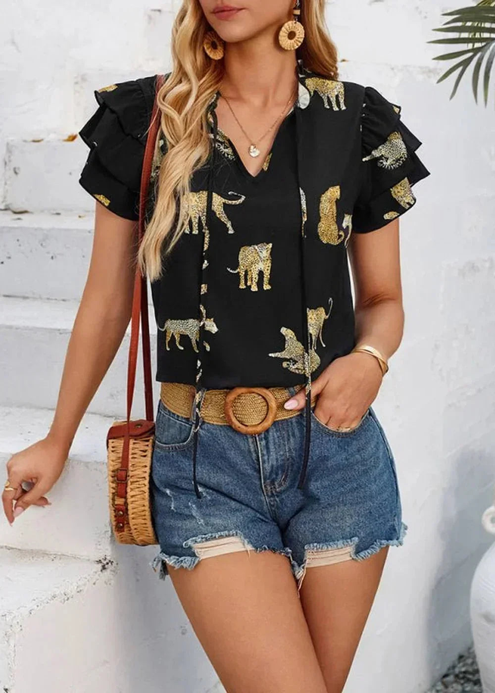 Black top with gold leopard print, ruffled cap sleeves, and tie neck, paired with distressed denim shorts.