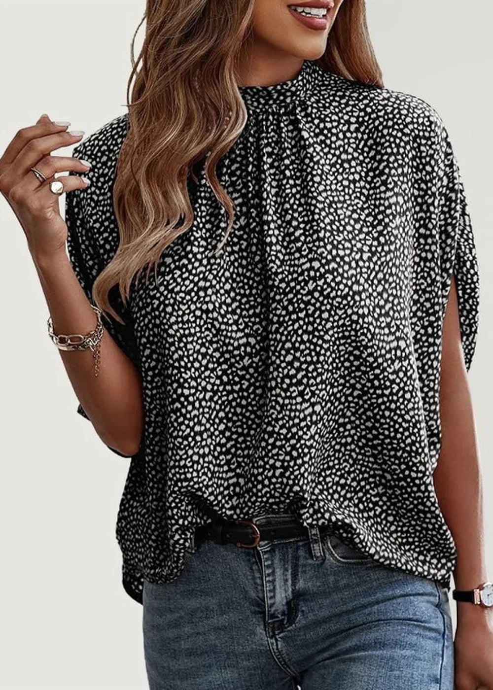 Black and white speckled print top with mock neck and short sleeves, worn with blue jeans and a black belt.