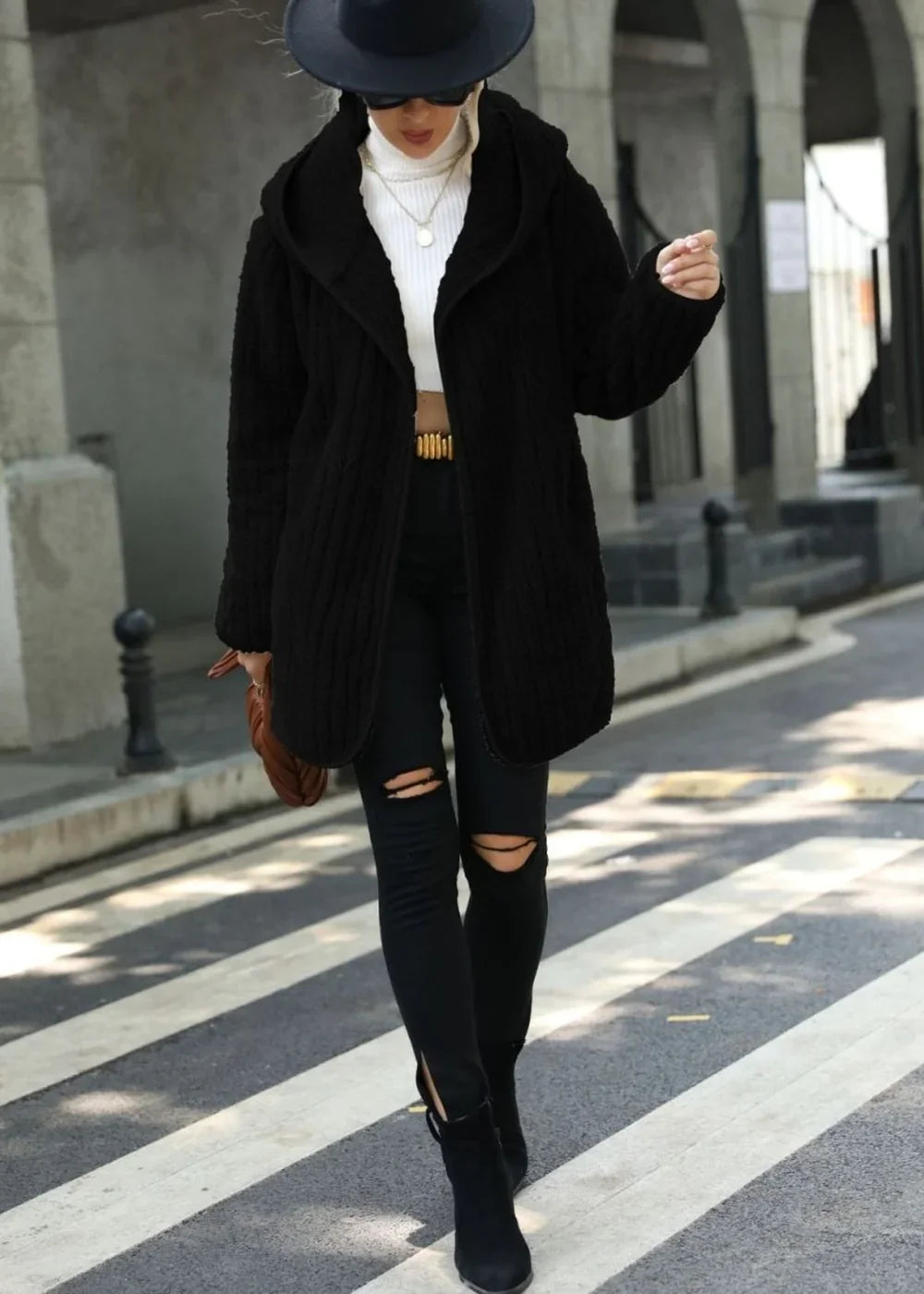 Black textured hooded coat with a relaxed fit, worn over a white turtleneck and ripped black jeans.