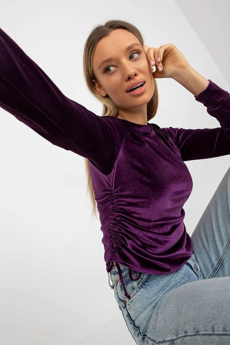 Deep purple velvet long-sleeve top with ruched side detail and adjustable drawstring, paired with light-wash denim jeans.