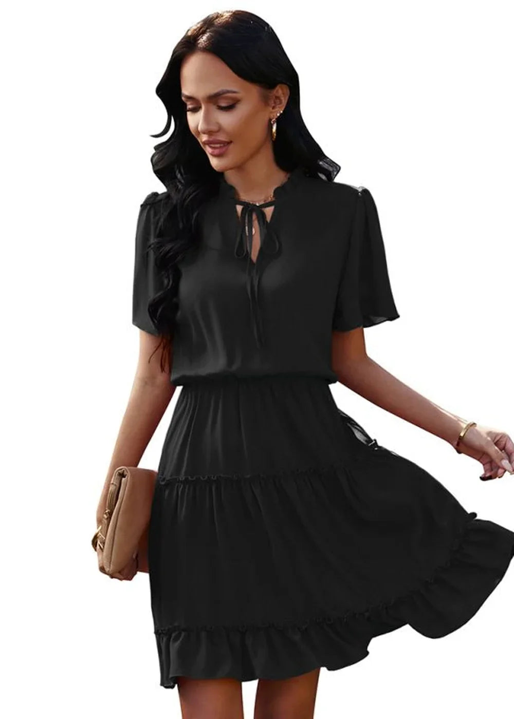 Black ruffled tiered dress with tie-neck and flutter sleeves, held by a model with a tan clutch.