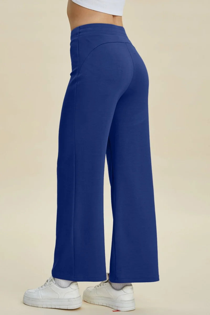 Side view of navy blue wide-leg pants with a smooth texture, worn with white sneakers.