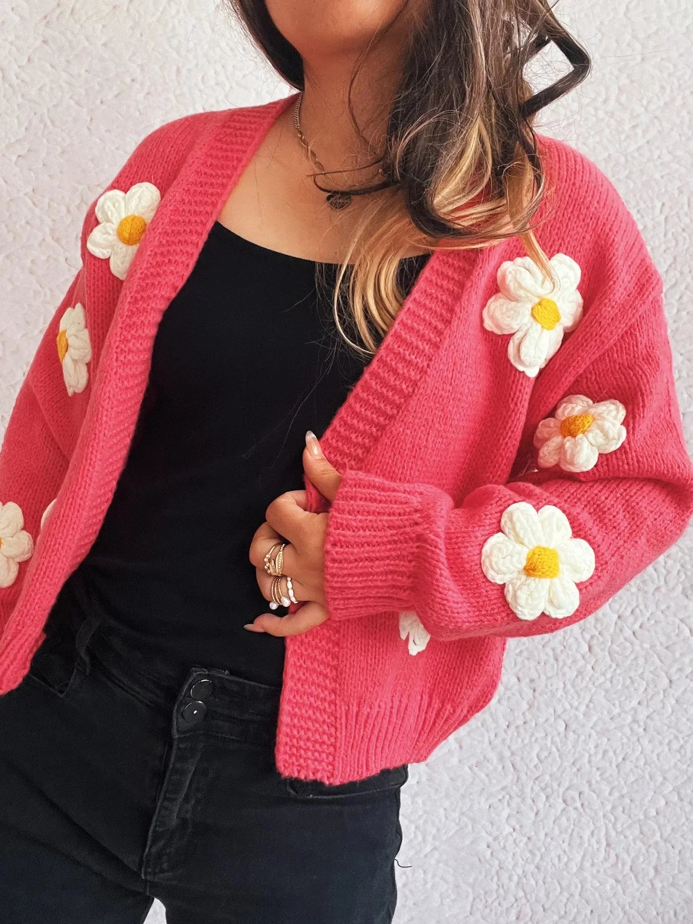 Pink knit cardigan with 3D white and yellow flowers, black top, and black jeans.