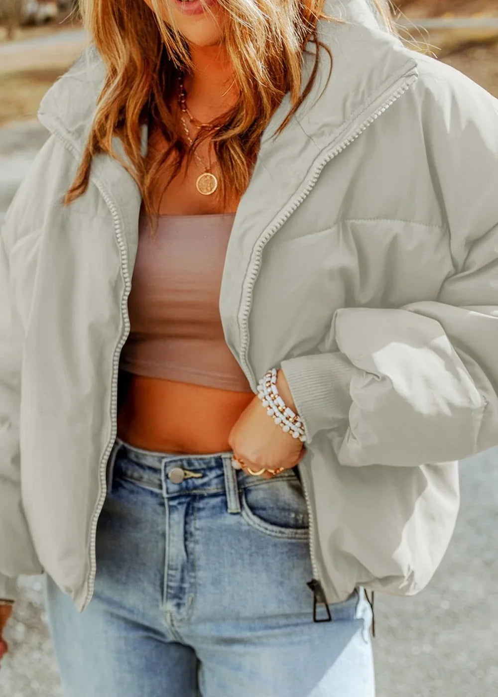 Light grey puffer jacket with a zipper closure and a soft sheen, worn by a model with a crop top and jeans.
