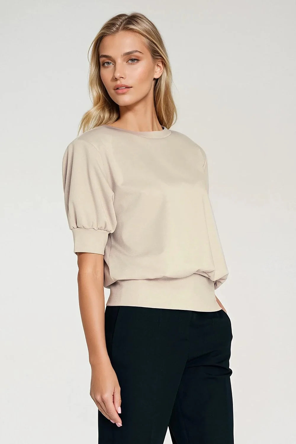 Model in oversized beige puff-sleeve top and black trousers.