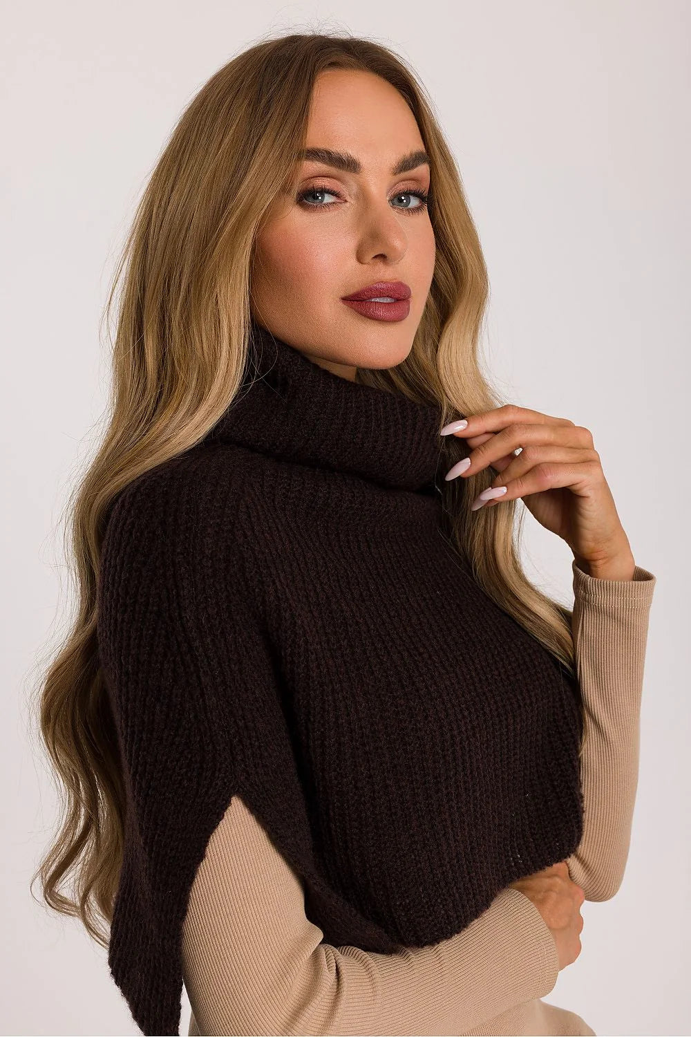 Woman with long blonde hair wearing a brown turtleneck poncho over a tan ribbed long-sleeve shirt.
