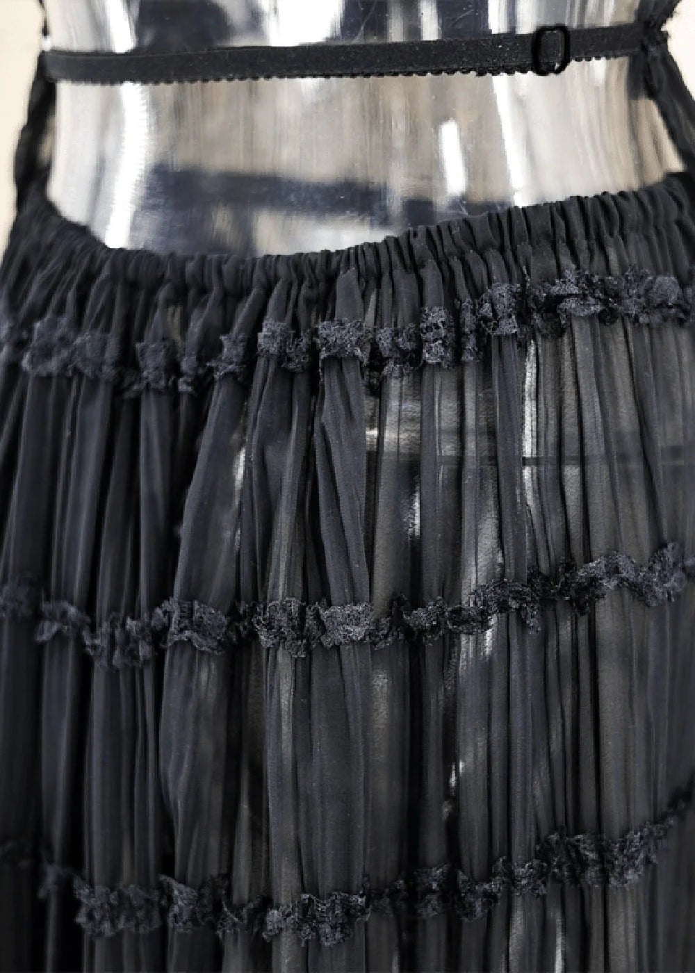 Black sheer tiered skirt with ruffled trim and elastic waistband on a mannequin.