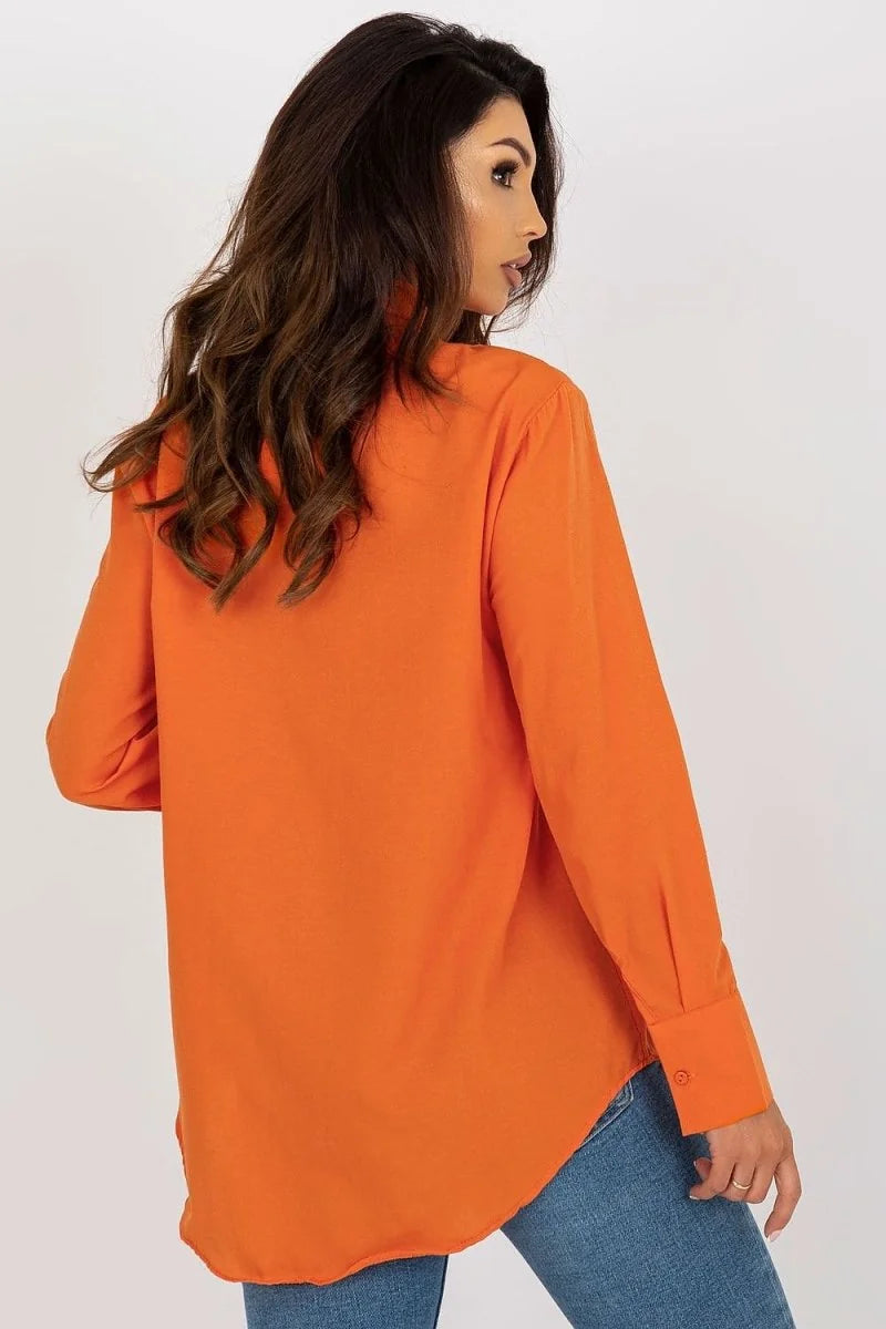Woman from behind wearing a loose-fit, bright orange long-sleeve shirt and blue jeans.