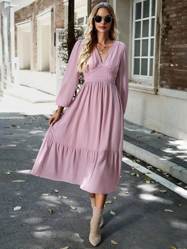 A woman models a flowy, dusty rose midi dress with a V-neck, lace trim, and tiered skirt.