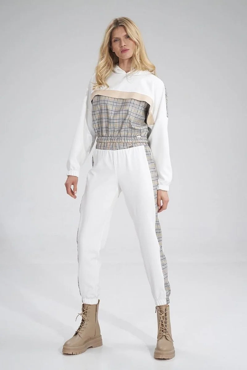 Full-length view of a woman wearing a white hooded tracksuit with plaid panels and tan accents, paired with tan combat boots.