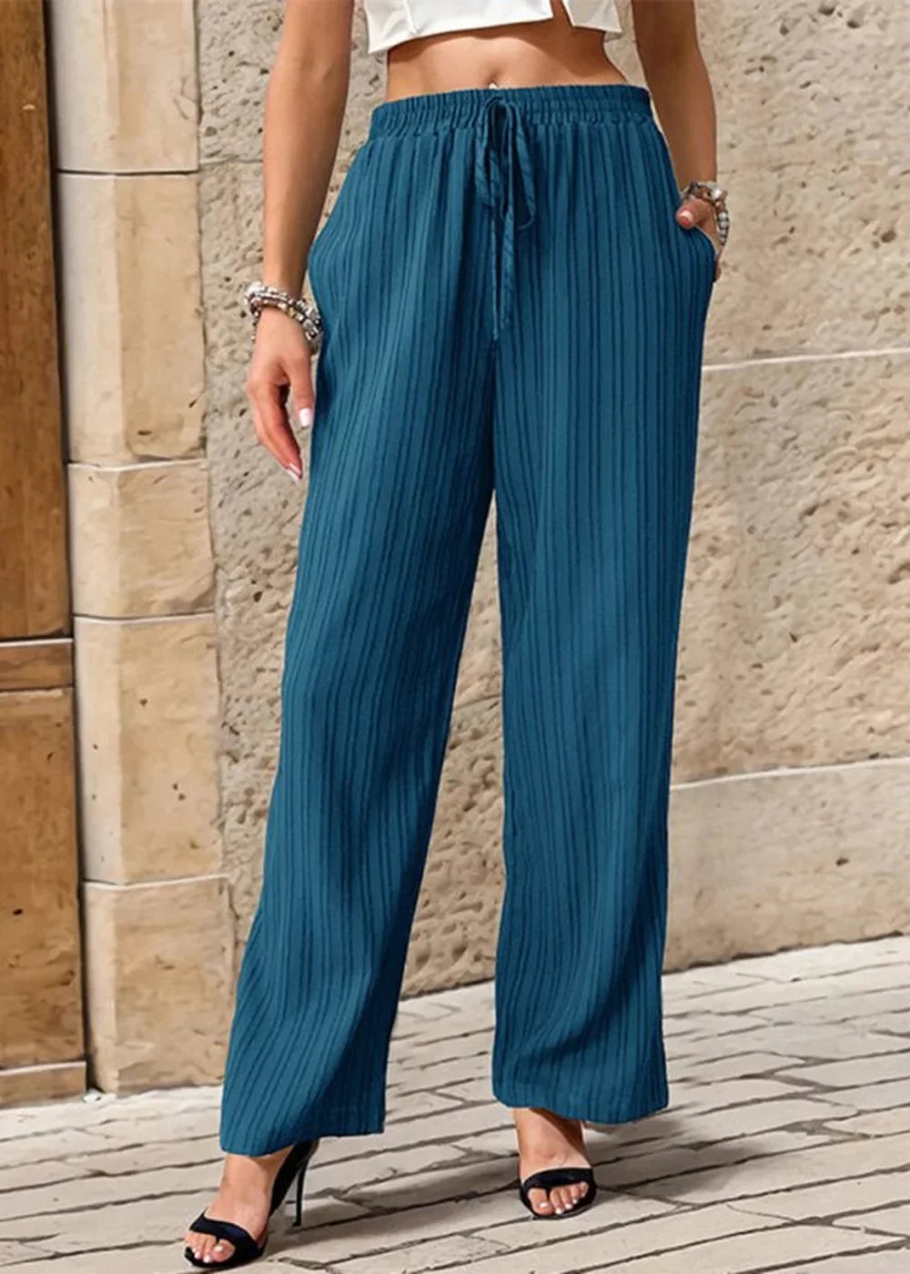 Teal pleated wide-leg pants with a drawstring waist and pockets, shown on a model.