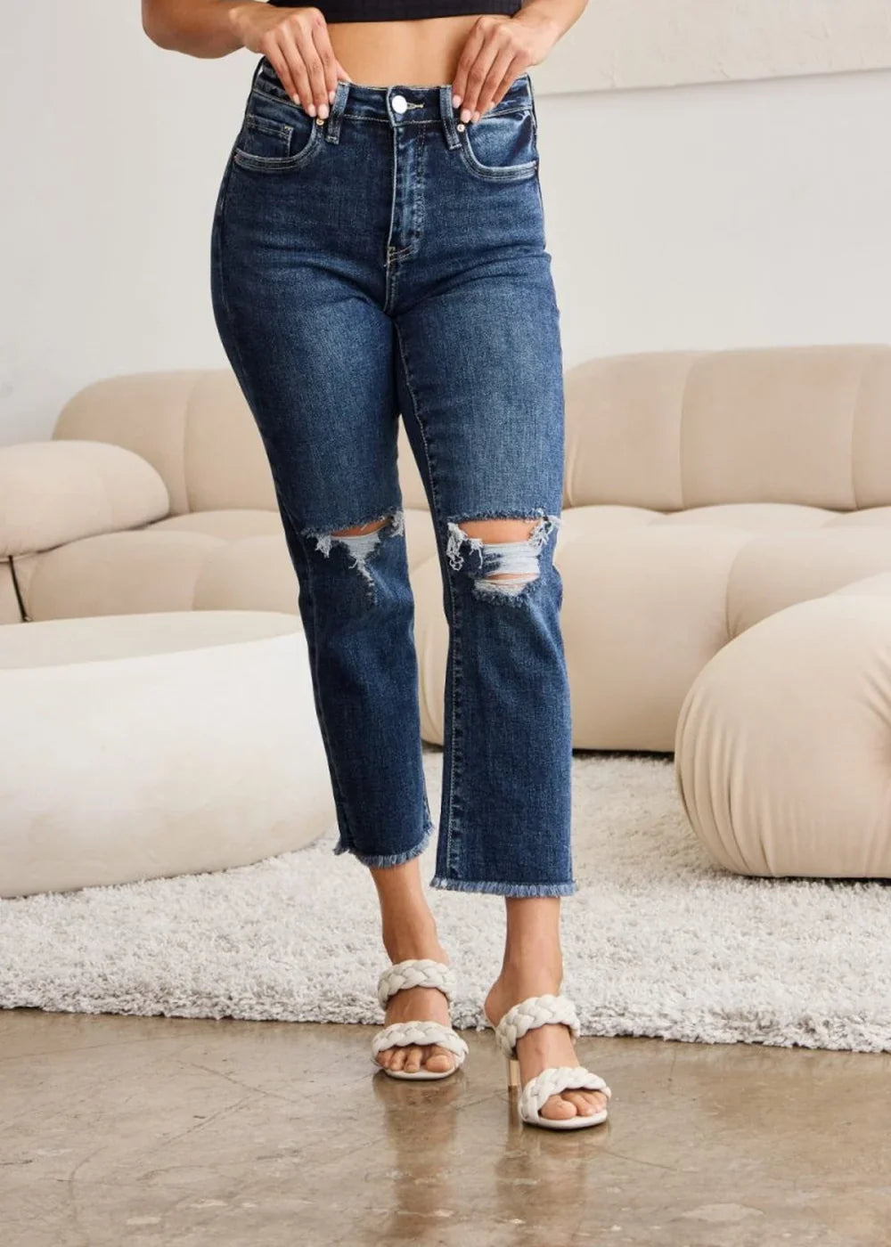 Distressed dark wash denim jeans with a frayed hem and ripped knees, worn by a model.