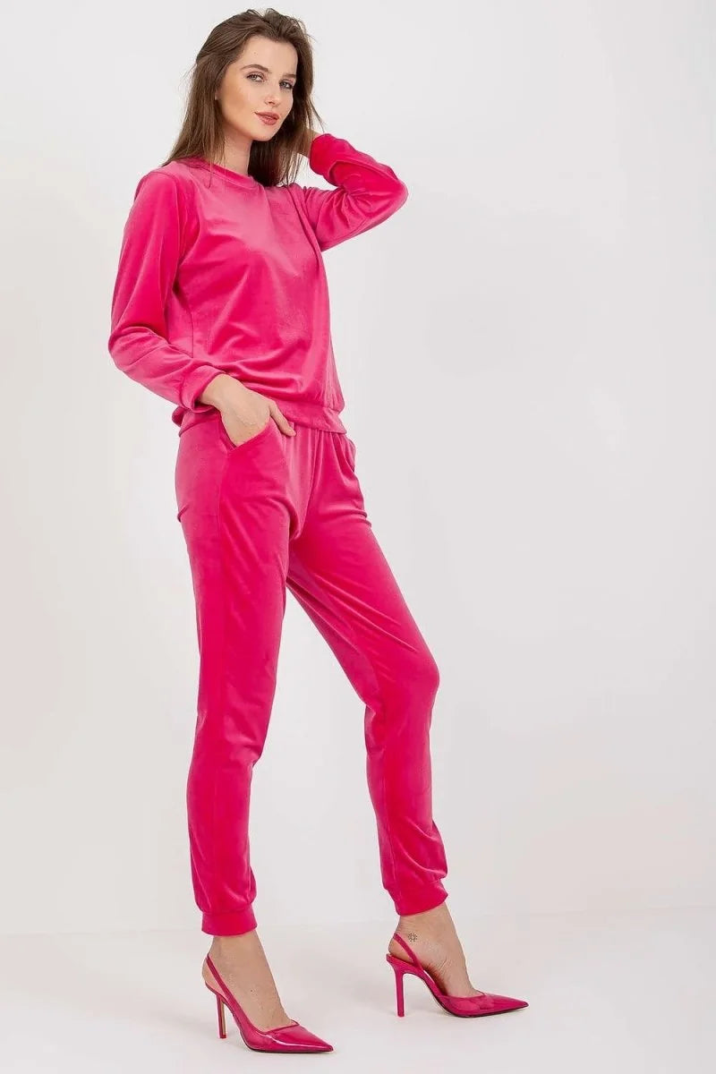 A woman in a vibrant pink velvet tracksuit and matching heels poses against a white background.