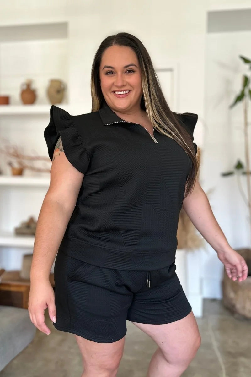 Black textured short suit with ruffled short sleeves and zip-neck top.