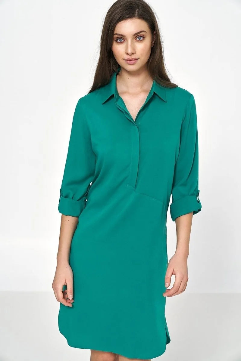 Woman in an oversized, emerald green viscose shirt dress with rolled-up sleeves.