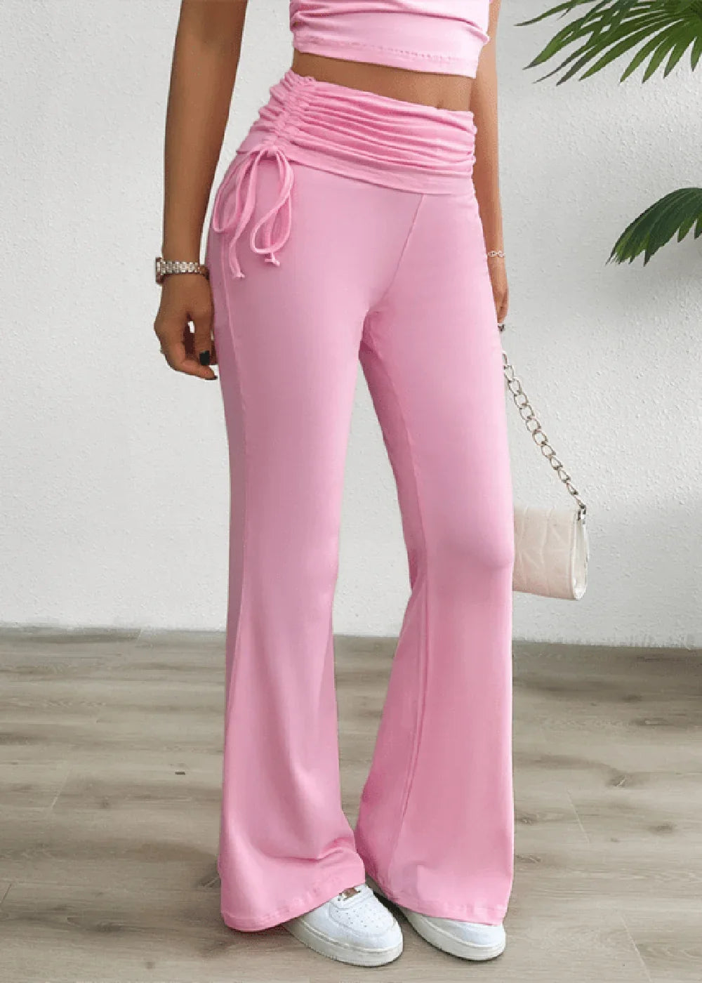 Pink flared pants with ruched drawstring waist and white sneakers on model.