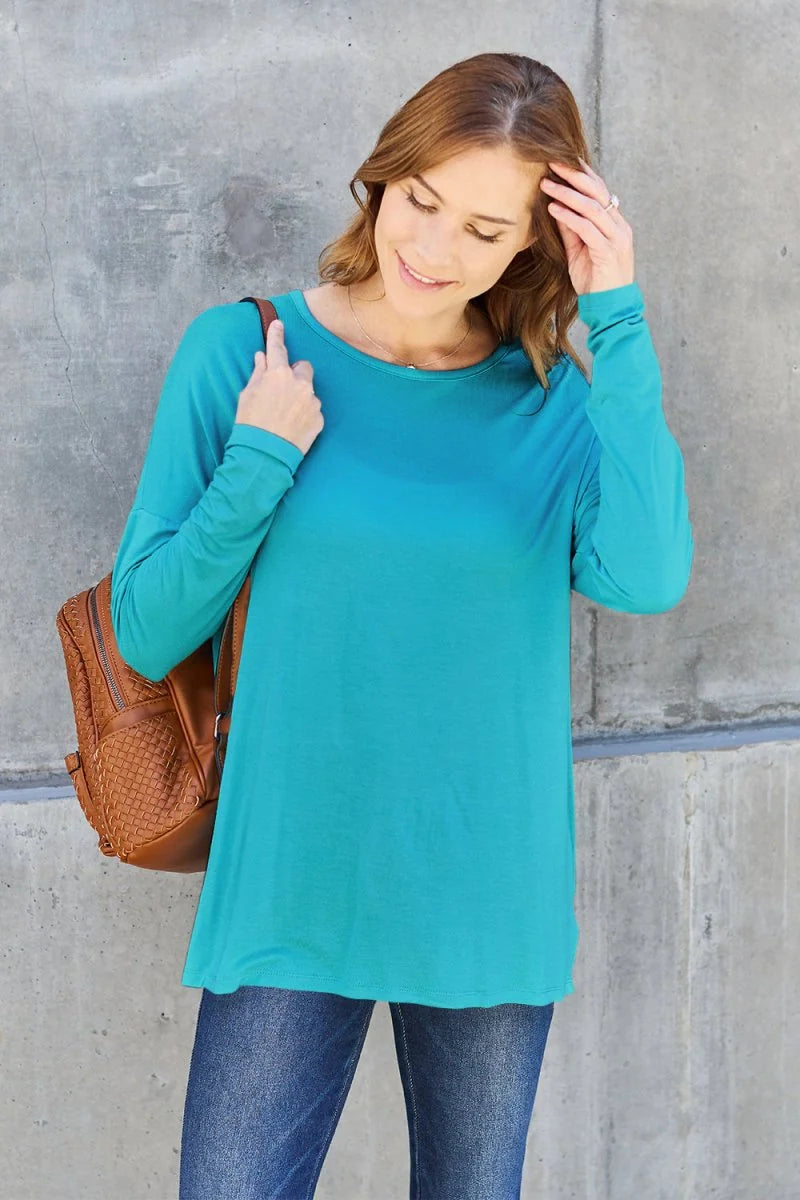 Teal long-sleeve tunic top with a rounded neckline, worn with blue jeans and a brown woven crossbody bag.
