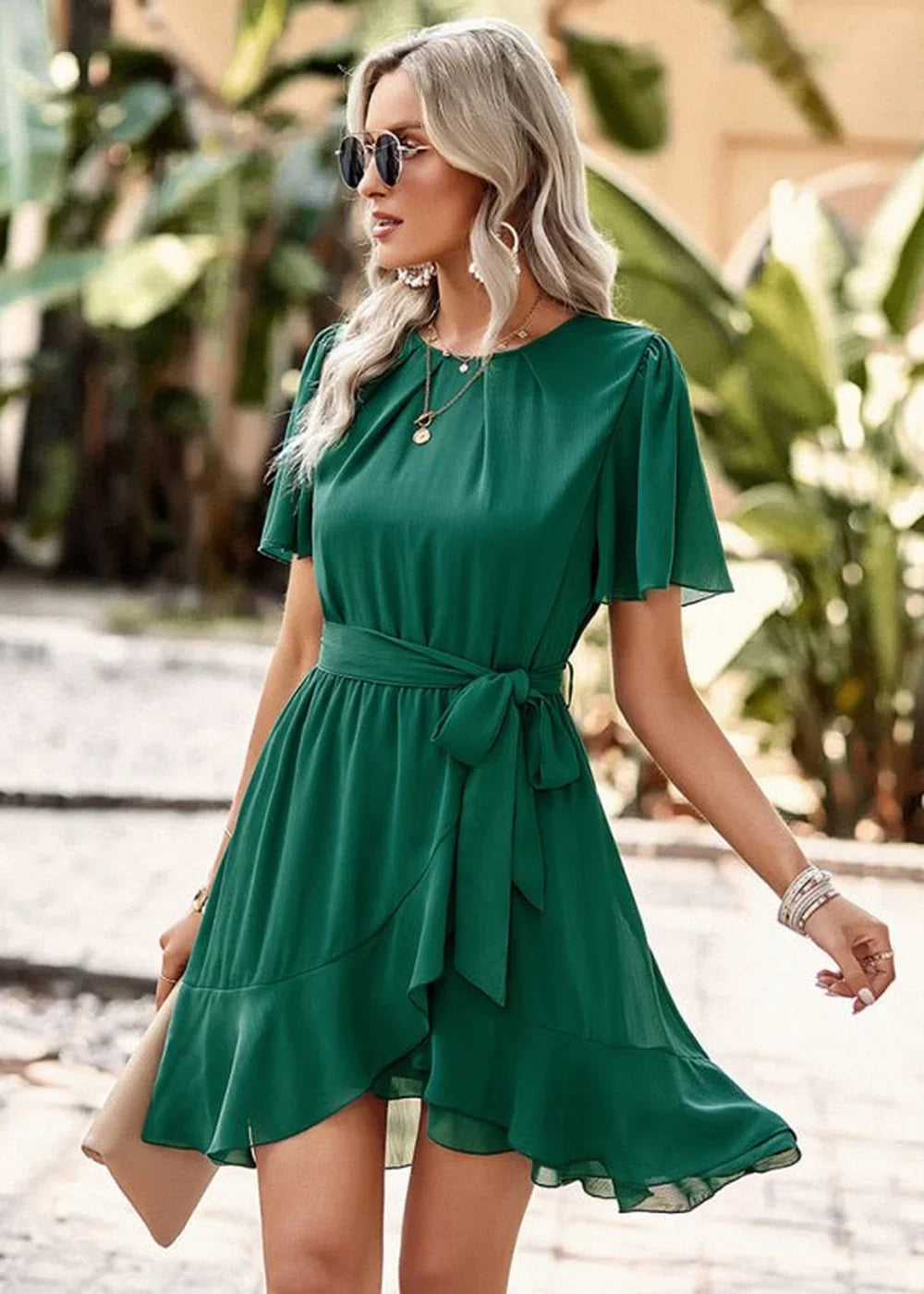 Emerald green faux wrap dress with flutter sleeves, a tie waist, and ruffled hem on model.